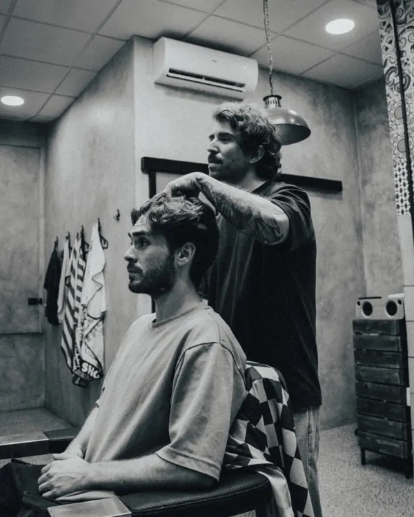 Pablo peinando a un cliente en el sillón, en blanco y negro